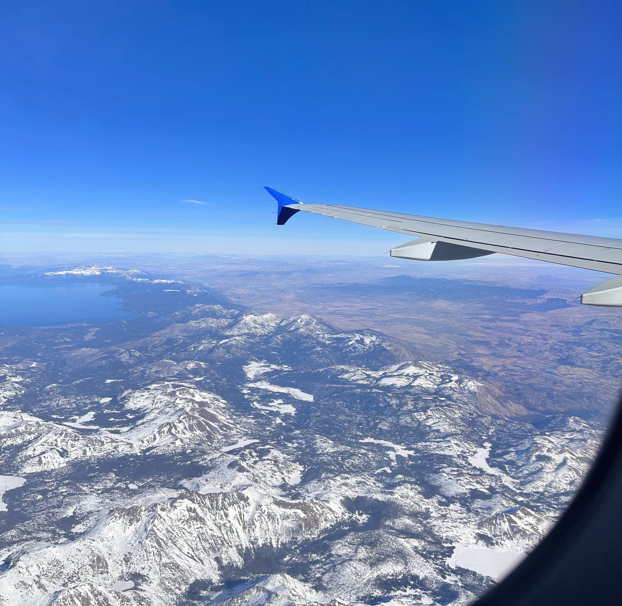 Photo taken from inside of an airplane flying over snow covered mountains. 
