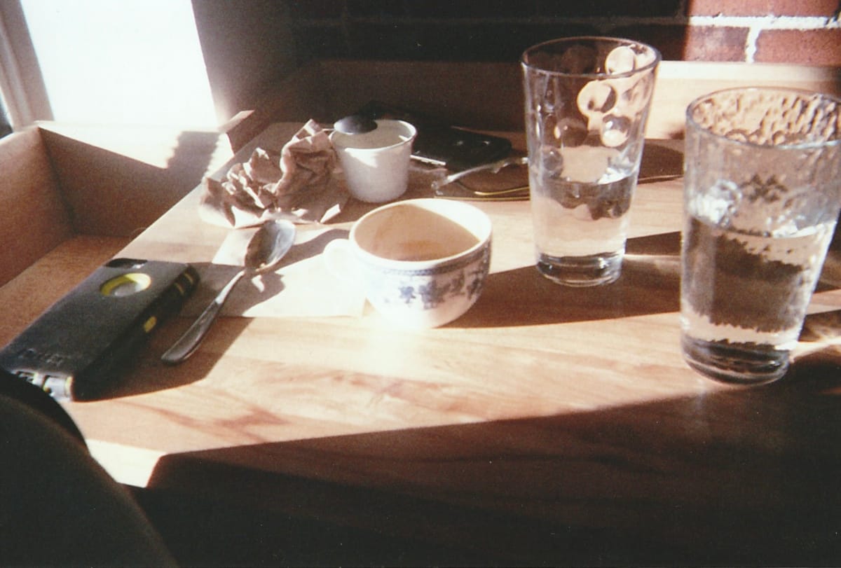 a messy table at a cafe shop taken from the perspective of the cafe guest. there's an iPhone facing down, two glasses of water, a mug, spoon, and napkins on the wooden table.